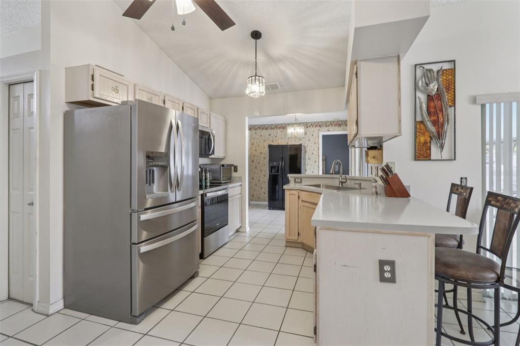 A kitchen with stainless steel appliances, light-colored cabinets, a breakfast bar, and tile flooring — 1977 S OLD MILL DRIVE, DELTONA, FL