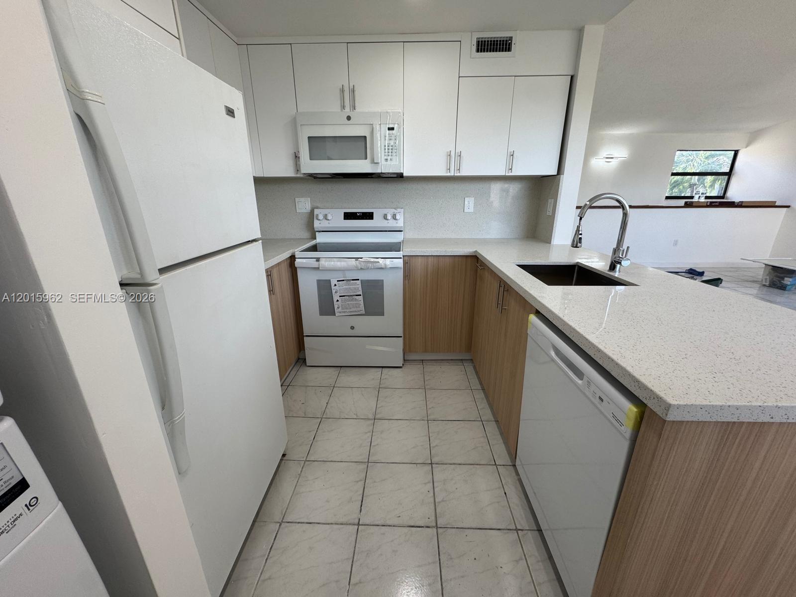 A kitchen features white upper cabinets, wood-toned lower cabinets, white appliances, and light-colored countertops — 10296 NW 9th St Cir # 202, Miami FL 33172, MIAMI, FL