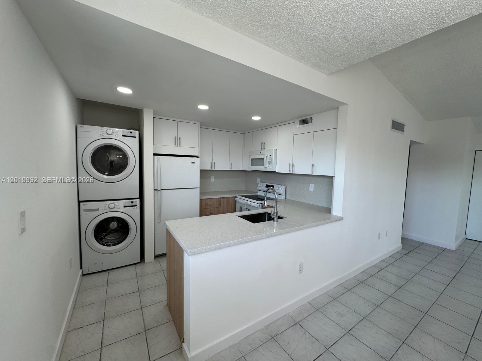A kitchen features white cabinets, a stacked washer and dryer, and a stone countertop — 10296 NW 9th St Cir # 202, Miami FL 33172, MIAMI, FL