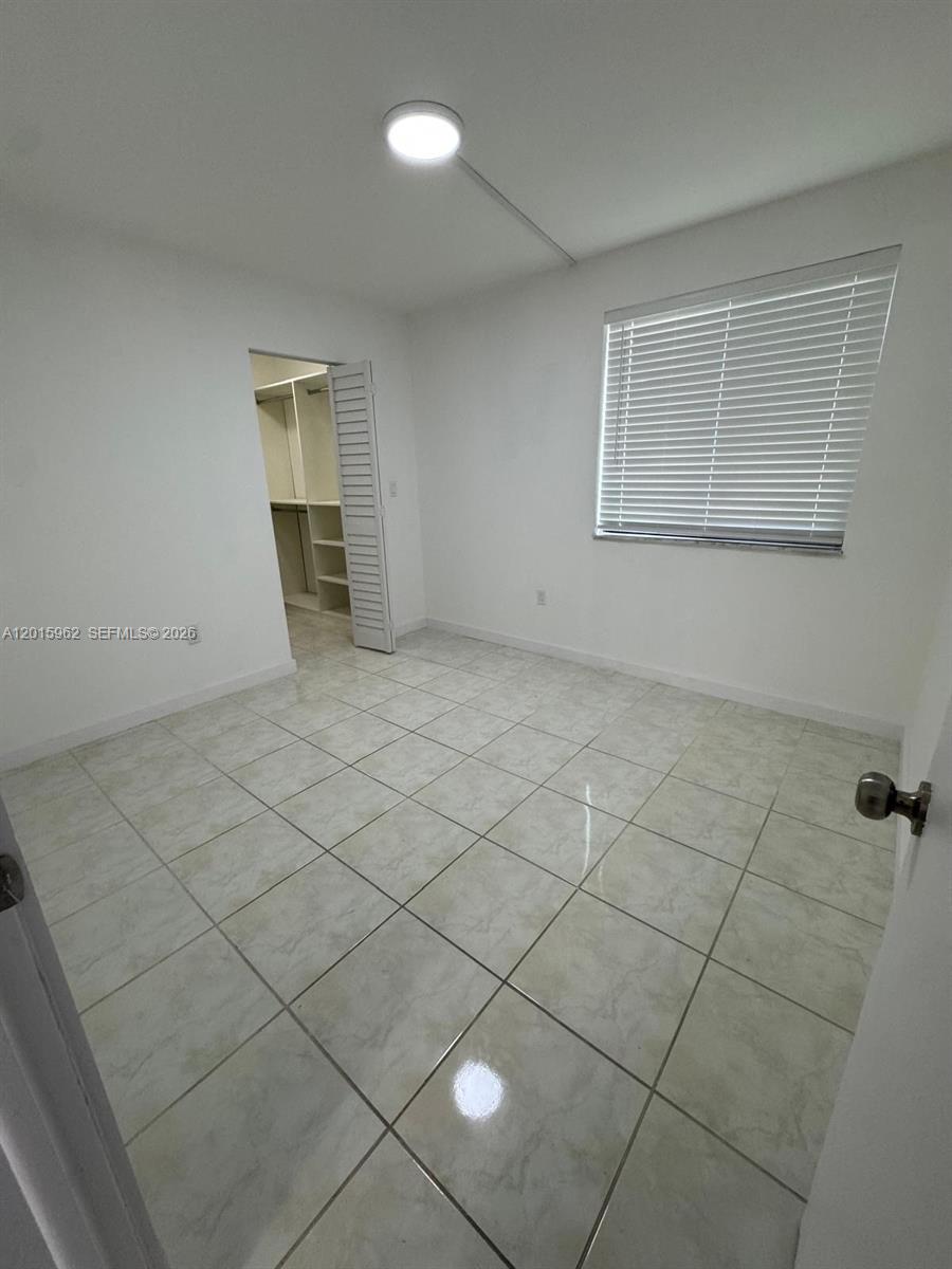 A bedroom with white walls, tiled floors, a window with blinds, and an open closet — 10296 NW 9th St Cir # 202, Miami FL 33172, MIAMI, FL