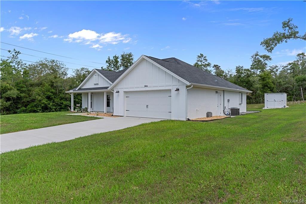 A white single-story house with a two-car garage and a detached shed on a lawn — 3004 WOODHILL STREET, INVERNESS, FL
