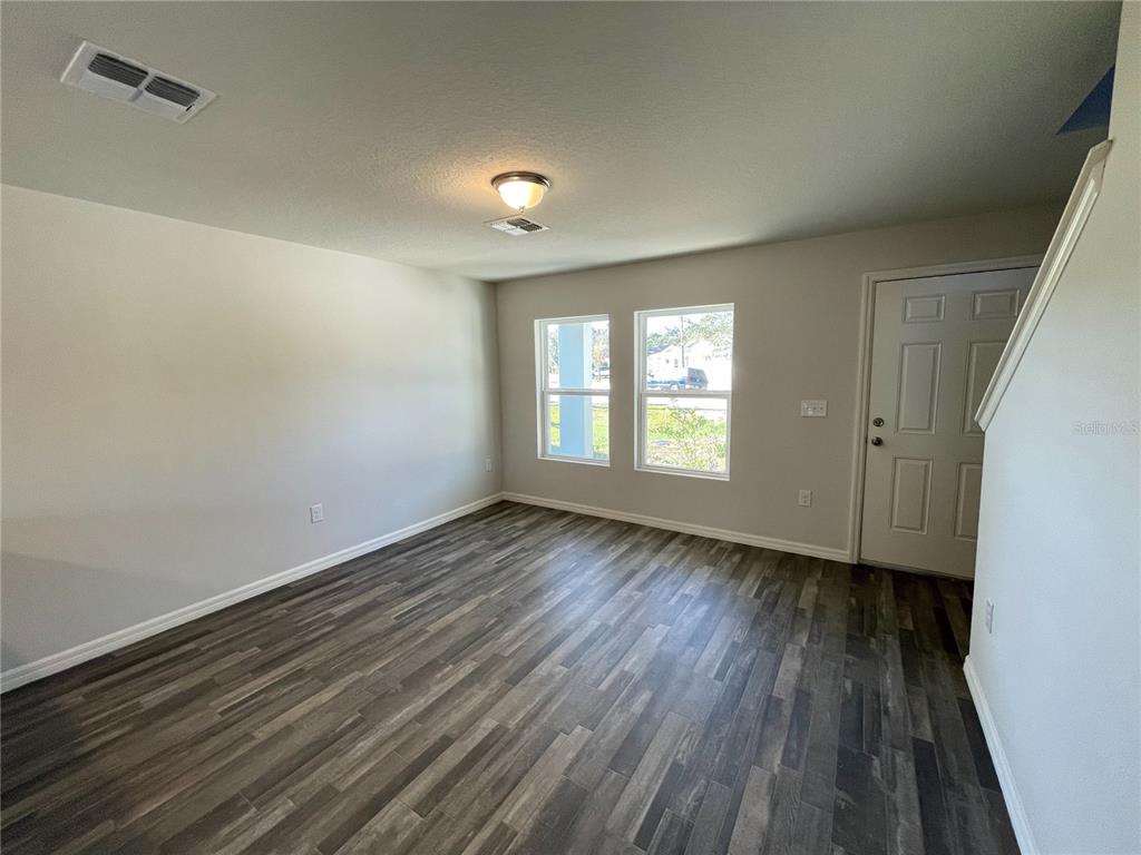 An empty room features wood-look flooring, light-colored walls, two windows, and a white entry door — 1630 TENCH COURT, KISSIMMEE, FL
