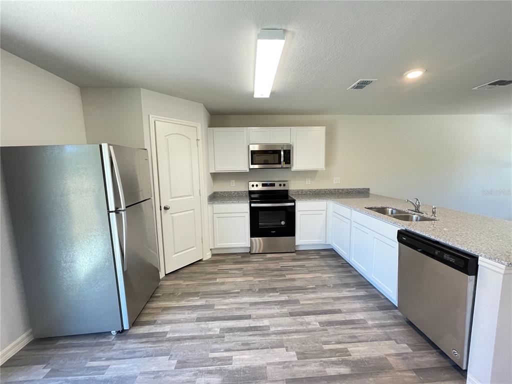 A kitchen features white cabinets, stainless steel appliances, granite countertops, and wood-look flooring — 1630 TENCH COURT, KISSIMMEE, FL