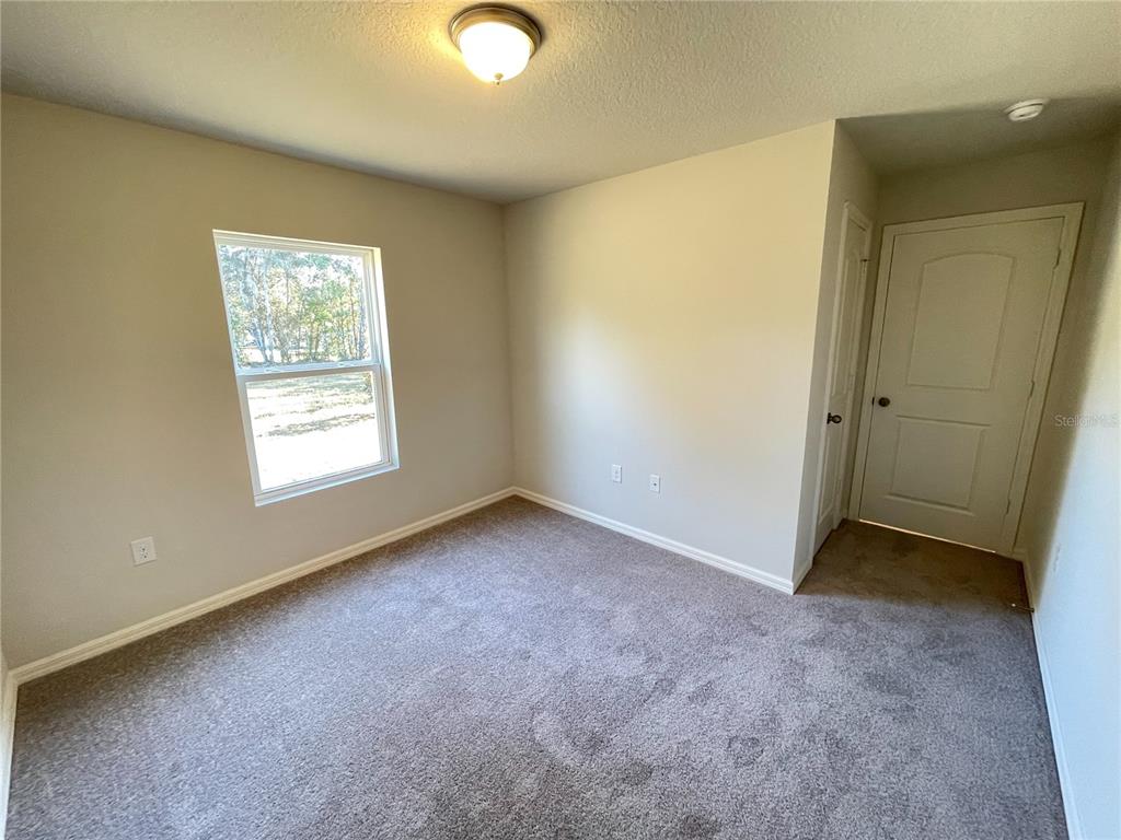 An empty bedroom features beige walls, gray carpeting, a single window, and a white door — 1630 TENCH COURT, KISSIMMEE, FL