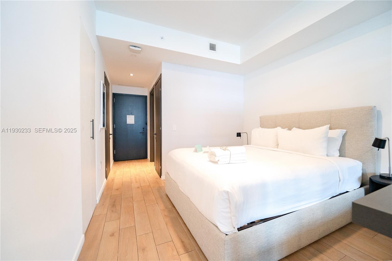 A bedroom features a bed with a beige headboard, light wood flooring, and white walls — 398 NE 5th St # 2602, Miami FL 33132, MIAMI, FL
