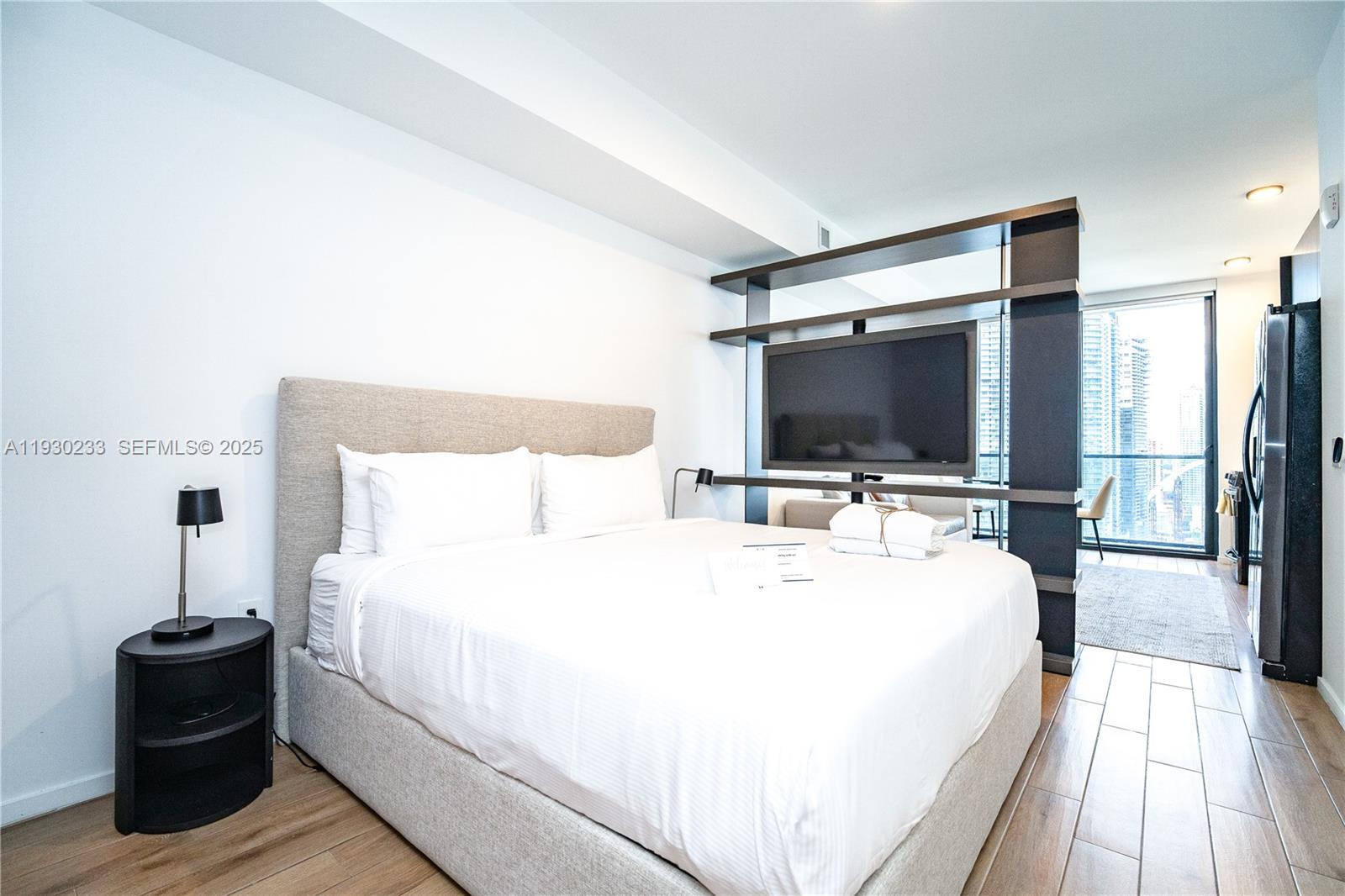 A bedroom features a bed, a room-dividing shelving unit with a television, and wood flooring — 398 NE 5th St # 2602, Miami FL 33132, MIAMI, FL