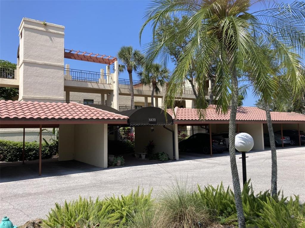 A multi-story apartment building features covered parking spaces with red tile roofs and palm trees — 6430 SUN EAGLE LANE UNIT 203, BRADENTON, FL