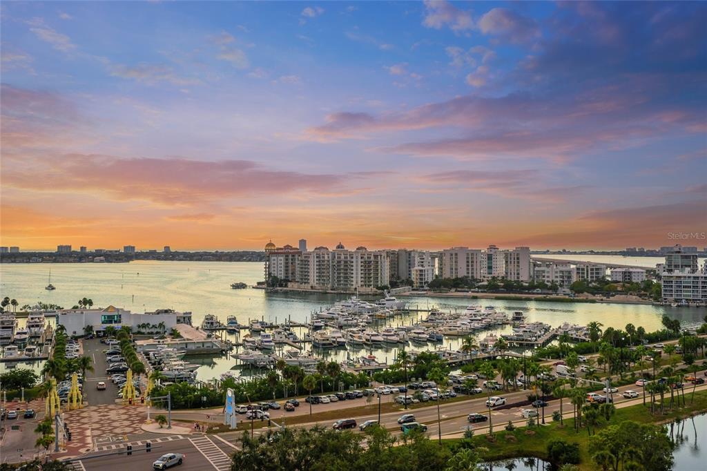 An aerial view shows a marina with many boats, waterfront buildings, and a sunset sky — 1330 MAIN STREET UNIT PH 9 & 10, SARASOTA, FL