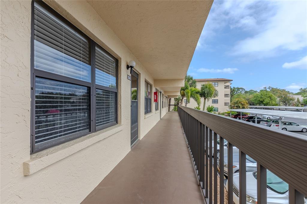 An exterior walkway leads past a unit door and windows along a multi-story apartment building — 305 30TH AVENUE W UNIT A208, BRADENTON, FL