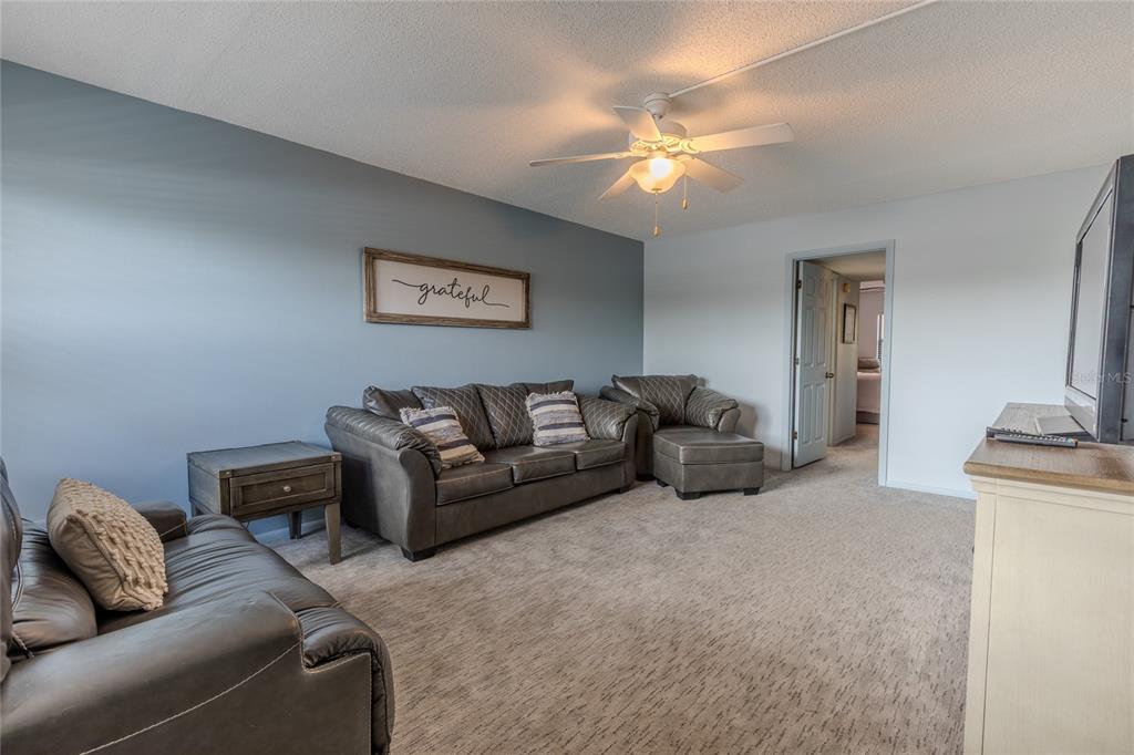 A living room features gray carpet, a blue accent wall, leather furniture, and a ceiling fan — 305 30TH AVENUE W UNIT A208, BRADENTON, FL
