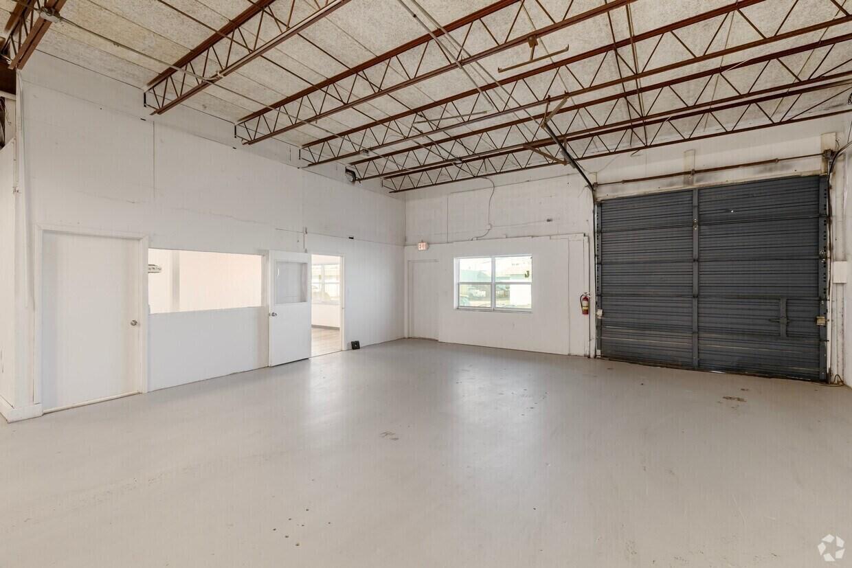 An empty industrial warehouse space features a concrete floor, exposed ceiling trusses, and a roll-up door — 400 NE 27th Street, Pompano Beach FL 33064, POMPANO BEACH, FL