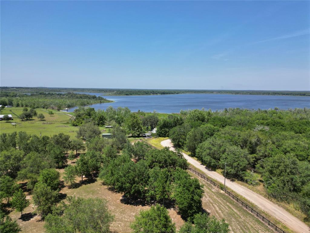 An aerial view shows a dirt road leading toward a lake surrounded by trees — TBD SE 55 PLACE, OCKLAWAHA, FL