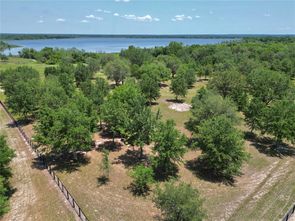 An aerial view shows a grassy, tree-filled lot bordering a large lake under a blue sky — TBD SE 55 PLACE, OCKLAWAHA, FL