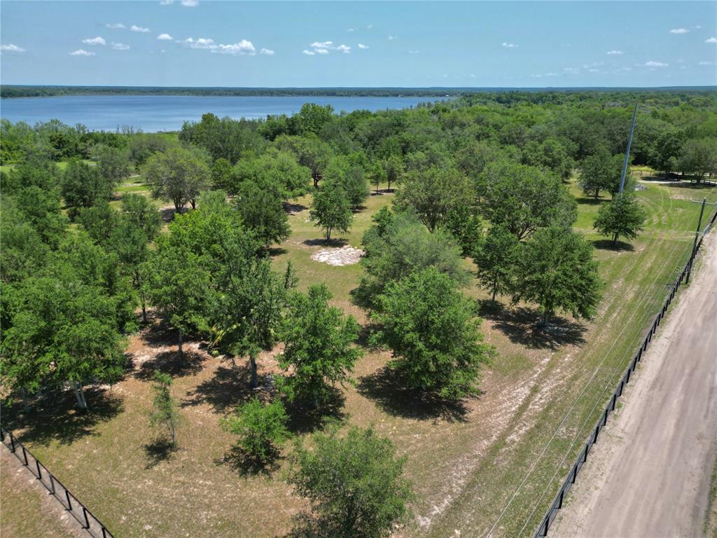 An aerial view shows a grassy, tree-filled lot bordering a lake next to a road — TBD SE 55 PLACE, OCKLAWAHA, FL
