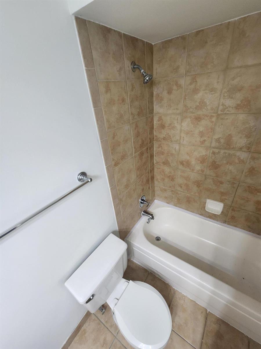 A bathroom features a white toilet, a chrome towel bar, and a tiled shower-tub combination — 1020 Crystal Way # F, Delray Beach FL 33444, DELRAY BEACH, FL