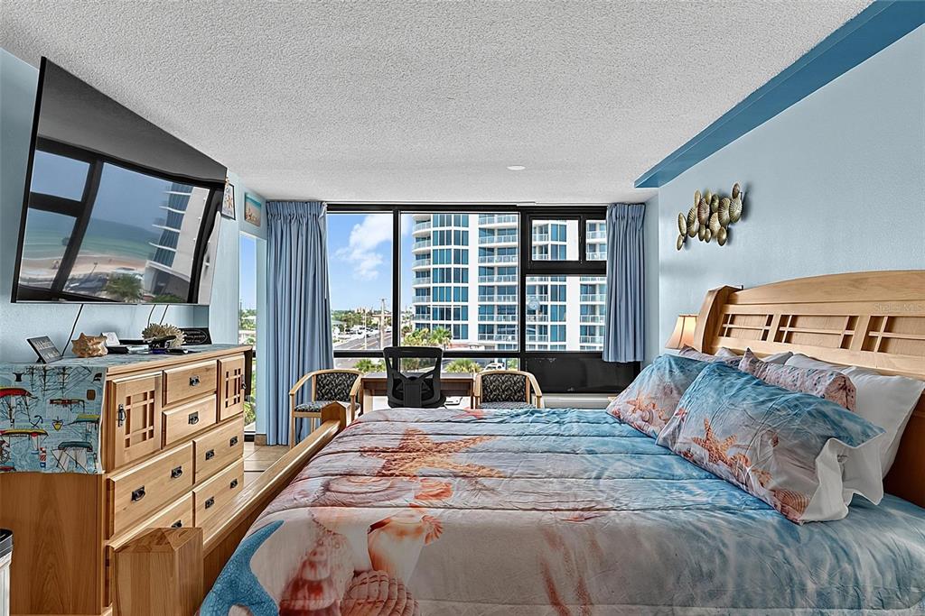 A bedroom with a bed, dresser, and large windows overlooking a coastal city — 1909 S ATLANTIC AVENUE UNIT 424, DAYTONA BEACH SHORES, FL