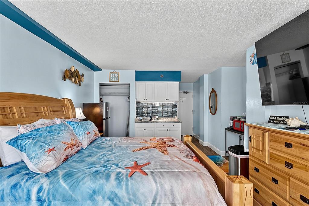 A bedroom features a wooden bed frame, a kitchenette, and a television mounted on the wall — 1909 S ATLANTIC AVENUE UNIT 424, DAYTONA BEACH SHORES, FL