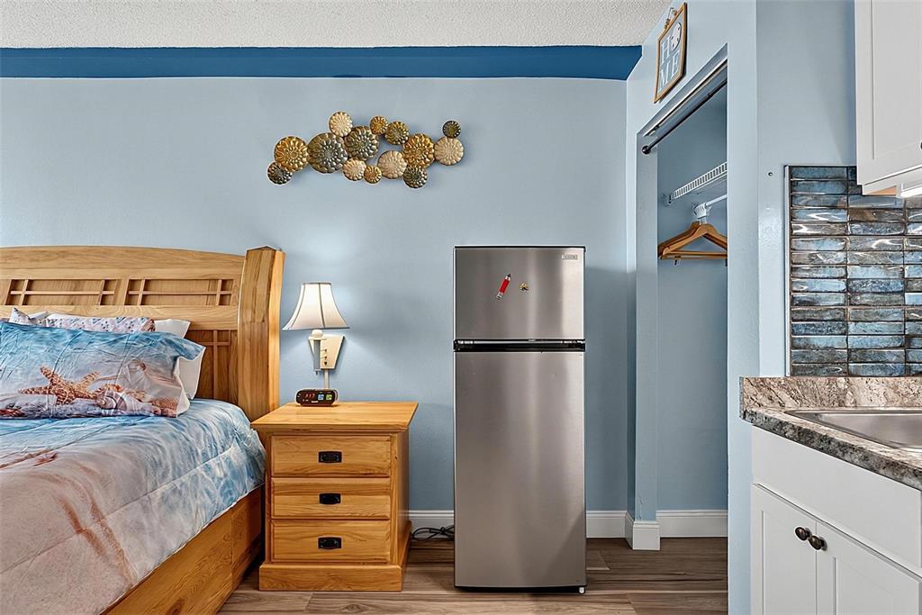 A bedroom with a wooden bed, nightstand, stainless steel refrigerator, and an adjacent kitchenette area — 1909 S ATLANTIC AVENUE UNIT 424, DAYTONA BEACH SHORES, FL