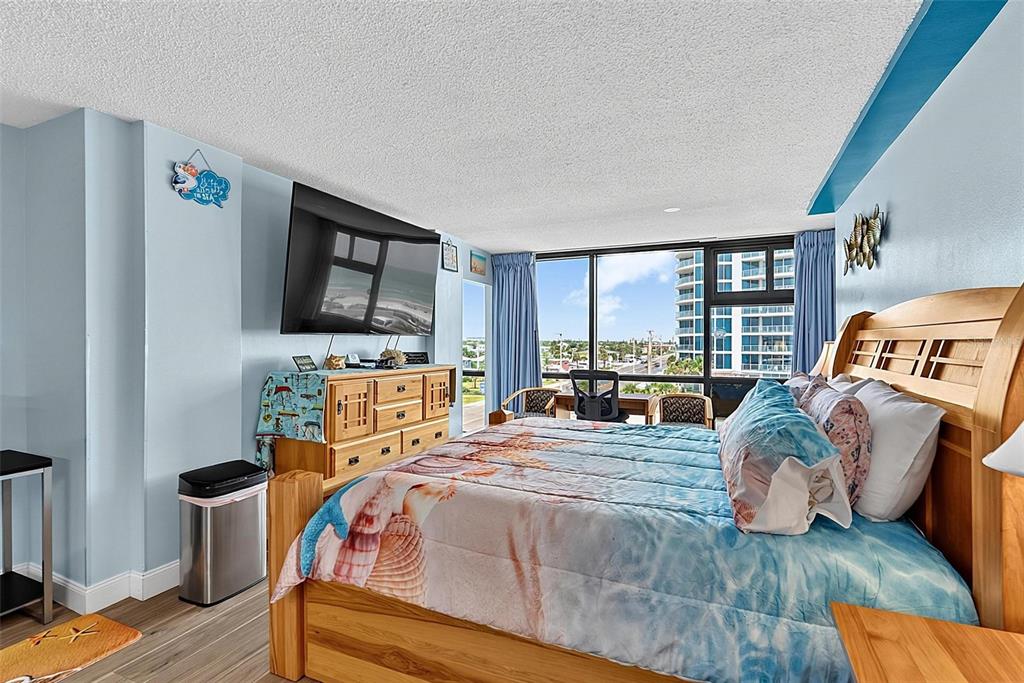 A bedroom features a wooden bed, a television mounted above a dresser, and floor-to-ceiling windows — 1909 S ATLANTIC AVENUE UNIT 424, DAYTONA BEACH SHORES, FL