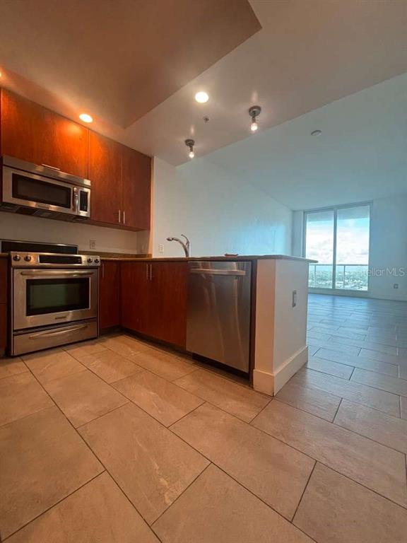 A kitchen with wood cabinets, stainless steel appliances, and tile flooring opens to a living area — 315 NE 3RD AVENUE UNIT 2009, FORT LAUDERDALE, FL