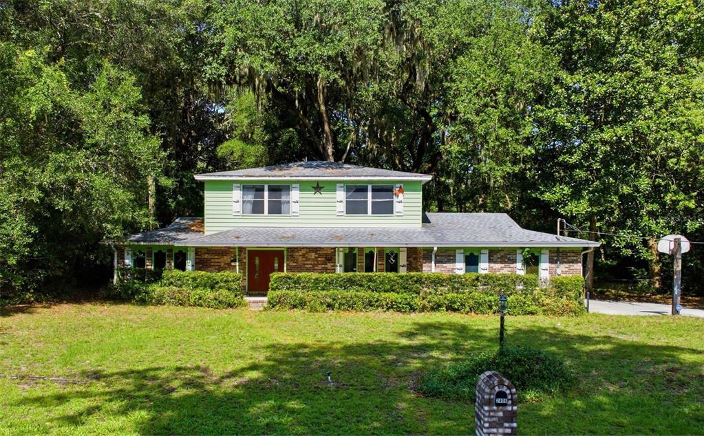 A two-story house with light green siding and a brick lower level sits among trees — 2406 ELBOW ROAD, ORANGE PARK, FL