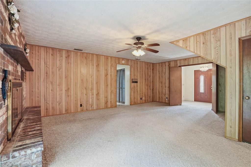A living room features wood-paneled walls, a brick fireplace, beige carpet, and a ceiling fan — 2406 ELBOW ROAD, ORANGE PARK, FL