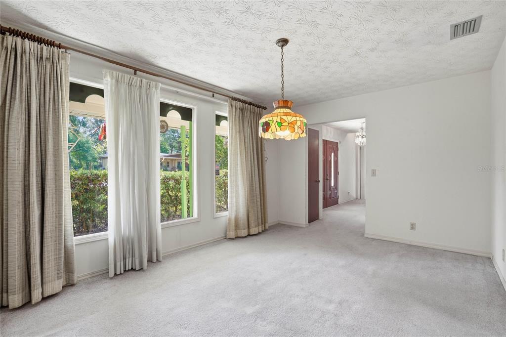 A carpeted dining room features a stained-glass pendant light and large windows with floor-length curtains — 2406 ELBOW ROAD, ORANGE PARK, FL
