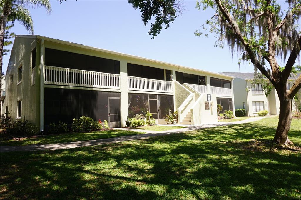 A two-story apartment building with screened balconies and a concrete staircase on a grassy lawn — 1775 CUPECOY CIRCLE UNIT O6, LUTZ, FL
