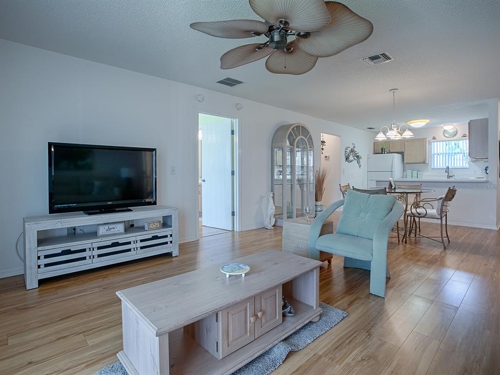 A living room with light wood flooring, a ceiling fan, and an open kitchen area — 3337 ASHBROOK PLACE, THE VILLAGES, FL