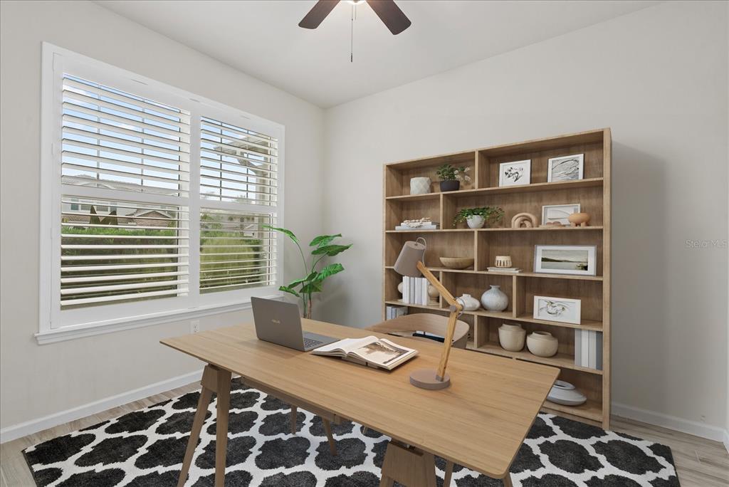 A home office features a wooden desk, a bookshelf, a patterned rug, and plantation shutters — 3331 CHESTERTOWN LOOP, BRADENTON, FL