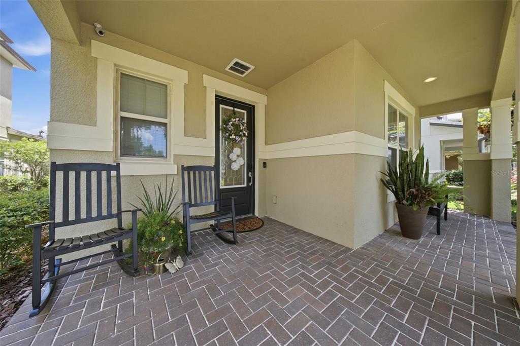 A covered front porch features brick pavers, two black rocking chairs, and a front door — 5920 VILLAGE CENTER DRIVE, LITHIA, FL