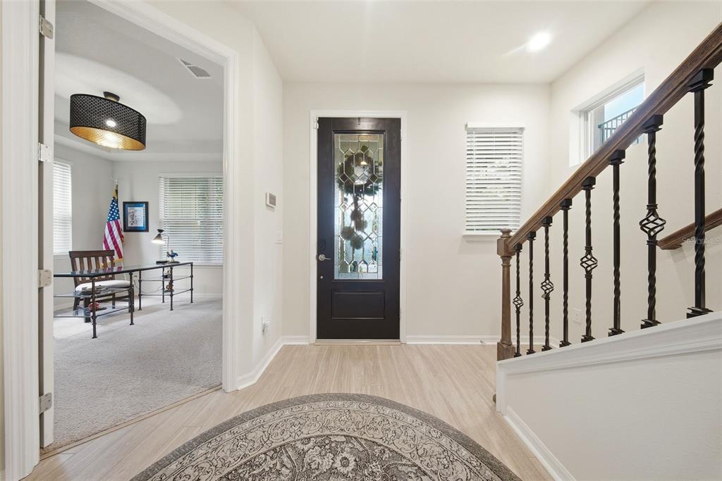 An entryway features light wood flooring, a dark front door, and a staircase with railings — 5920 VILLAGE CENTER DRIVE, LITHIA, FL