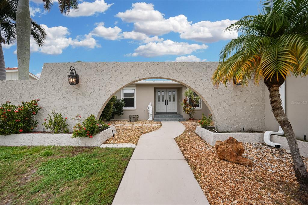 A concrete walkway leads through a large arched wall to the front entrance of a house — 931 BAL HARBOR BOULEVARD, PUNTA GORDA, FL