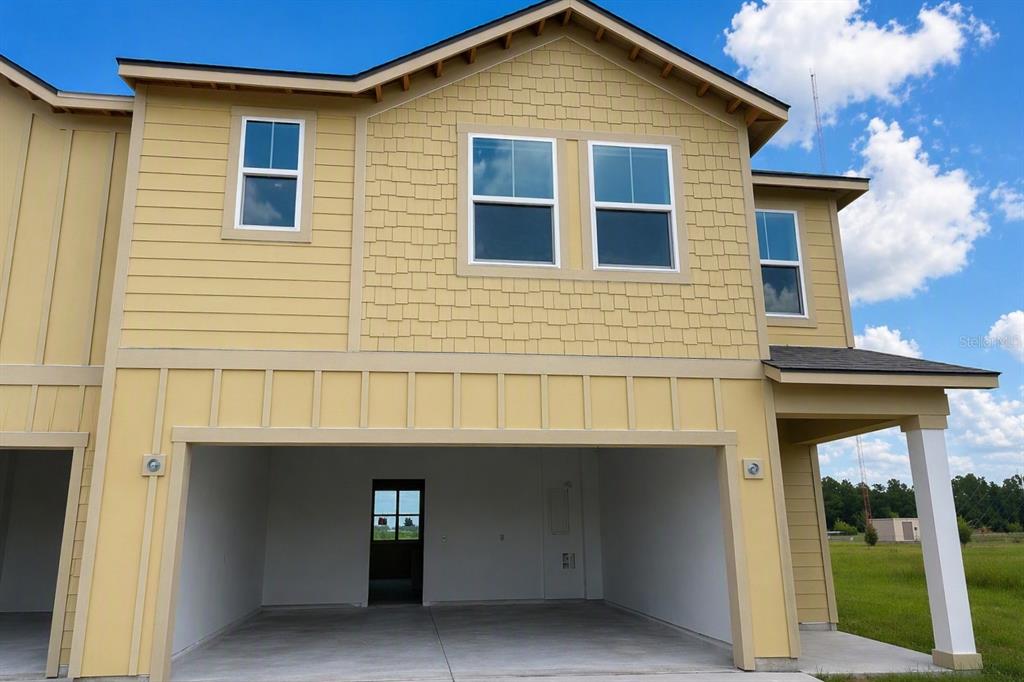 A yellow two-story house exterior featuring a large open garage and multiple windows — 7542 DEER VALLEY CIRCLE, TAMPA, FL
