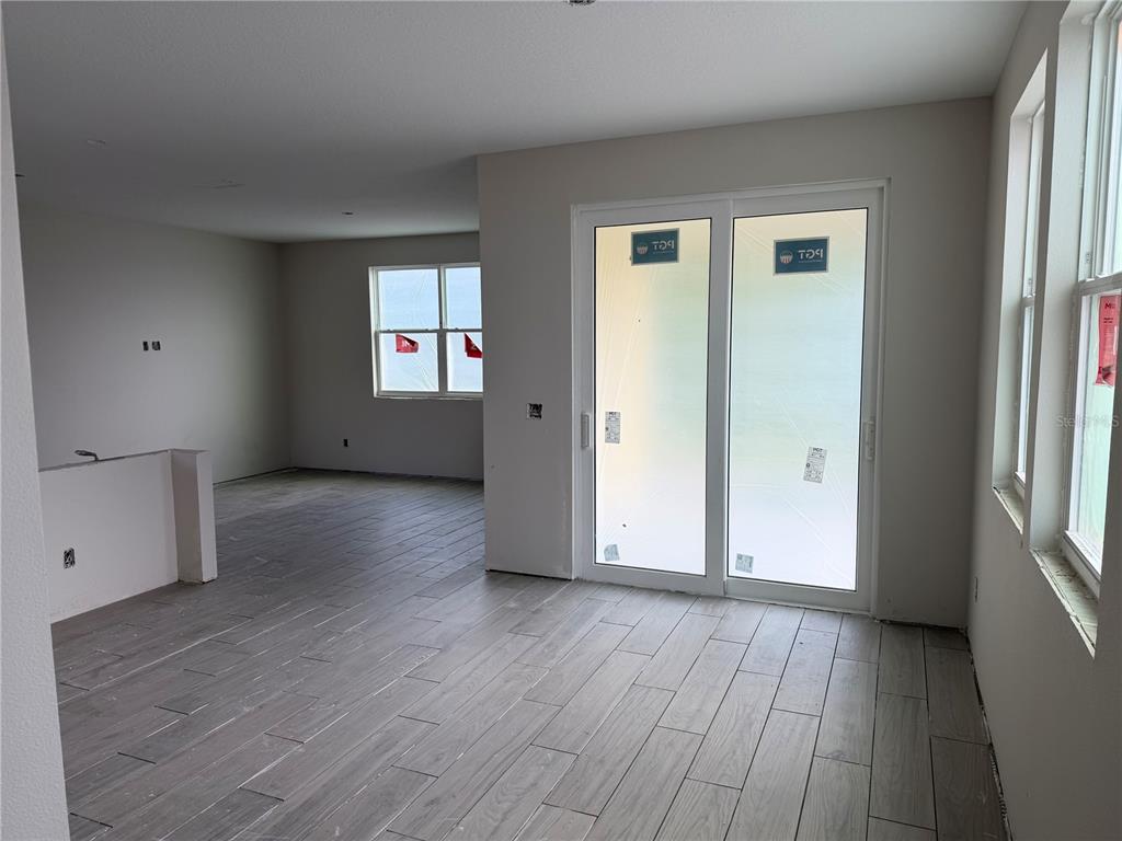 An unfinished room features light-colored wood-look tile flooring, sliding glass doors, and large windows — 7542 DEER VALLEY CIRCLE, TAMPA, FL