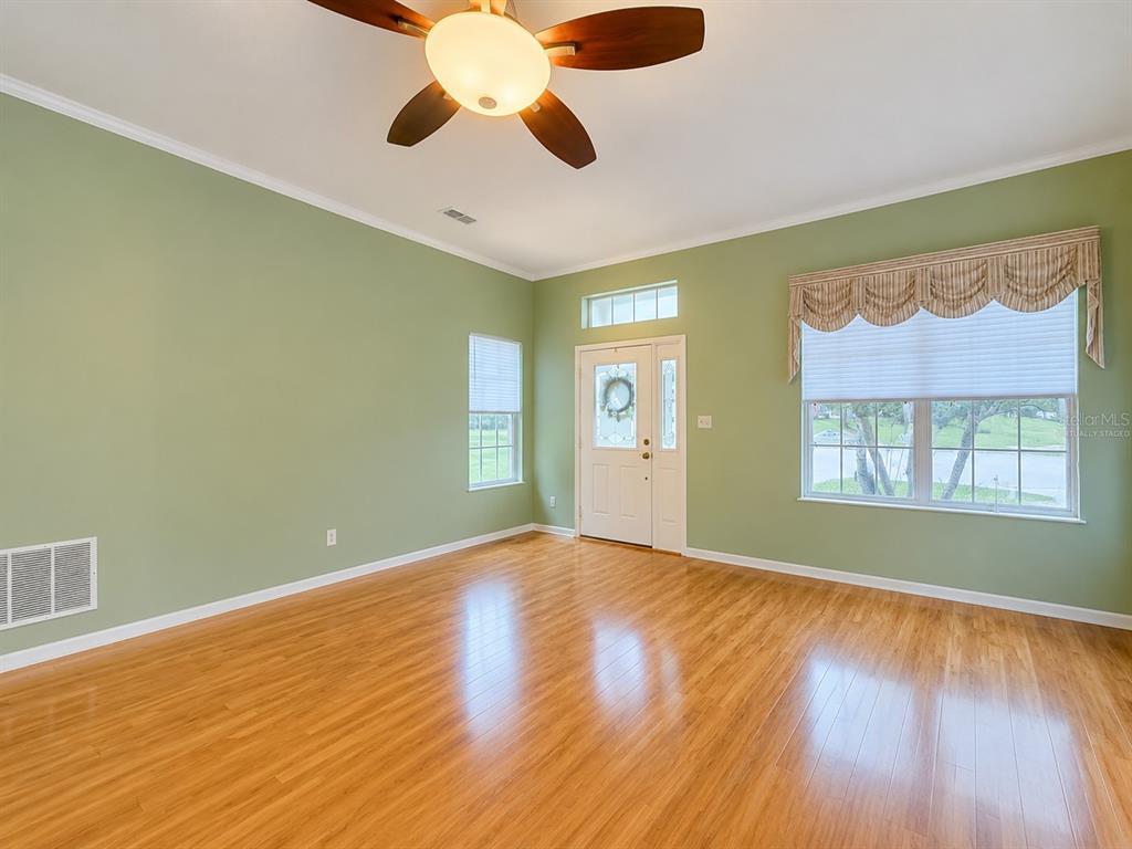 A living room with light green walls, wood flooring, a ceiling fan, and a front door — 4908 CYPRESS HEAD COURT, LEESBURG, FL