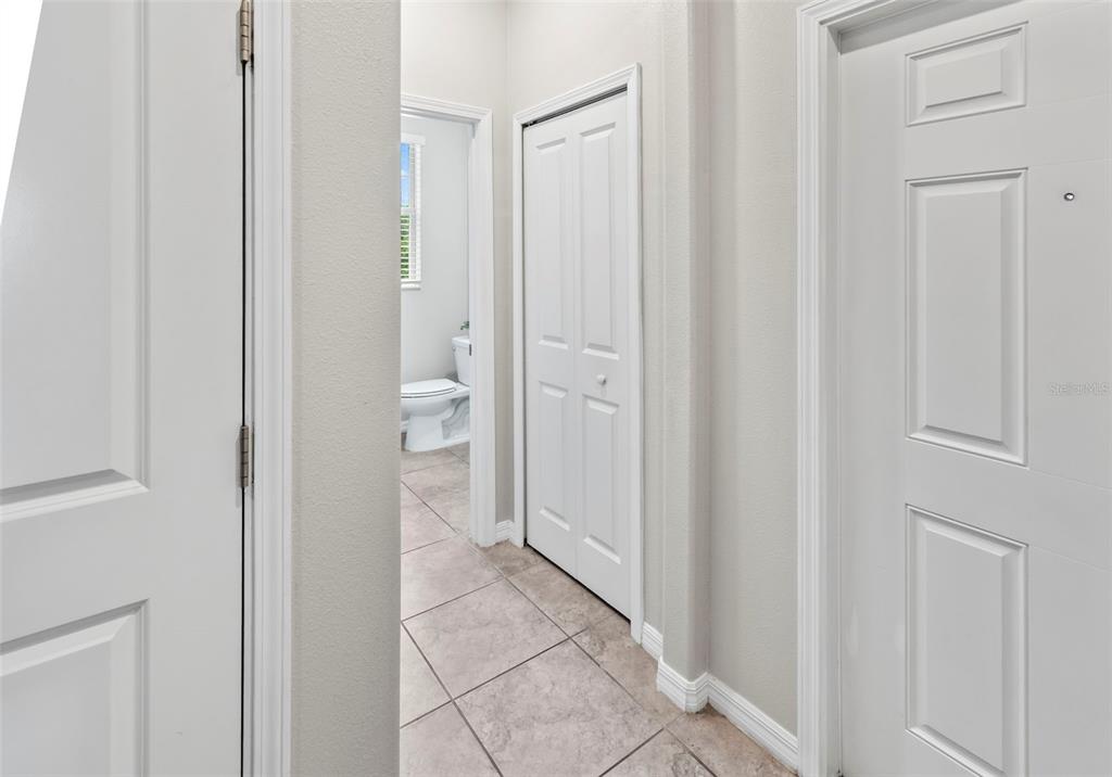 A hallway with tiled floors leads to a bathroom and features several white interior doors — 15504 FLORENCE HOLLOW PLACE, RUSKIN, FL