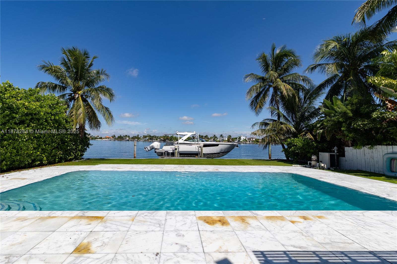 A rectangular swimming pool sits in front of a lawn with a boat docked nearby — 1215 N Biscayne Point Rd, Miami Beach FL 33141, MIAMI BEACH, FL