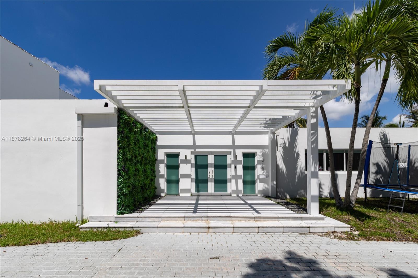 A modern white house entrance features a pergola, a green wall, and glass doors — 1215 N Biscayne Point Rd, Miami Beach FL 33141, MIAMI BEACH, FL