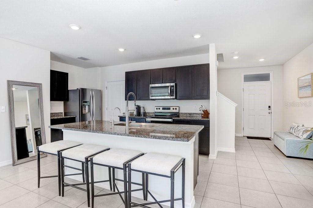 A kitchen features dark cabinets, granite countertops, a center island with stools, and tile flooring — 3044 SUNCOAST PLAINS DRIVE, ODESSA, FL