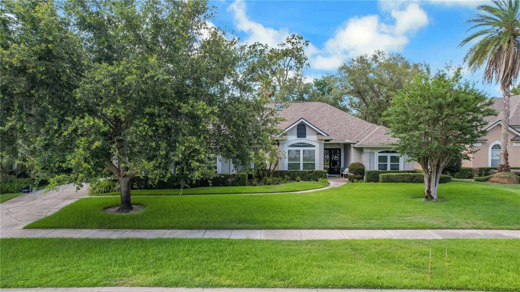 A single-story house with a lawn, trees, and a concrete driveway under a blue sky — 365 WOLDUNN CIRCLE, LAKE MARY, FL