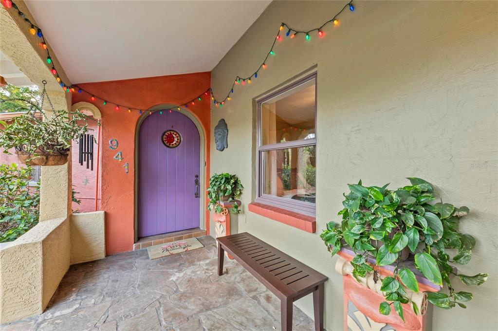 A covered porch features a purple arched door, stone flooring, a wooden bench, and string lights — 941 VIRGINIA DRIVE, SARASOTA, FL