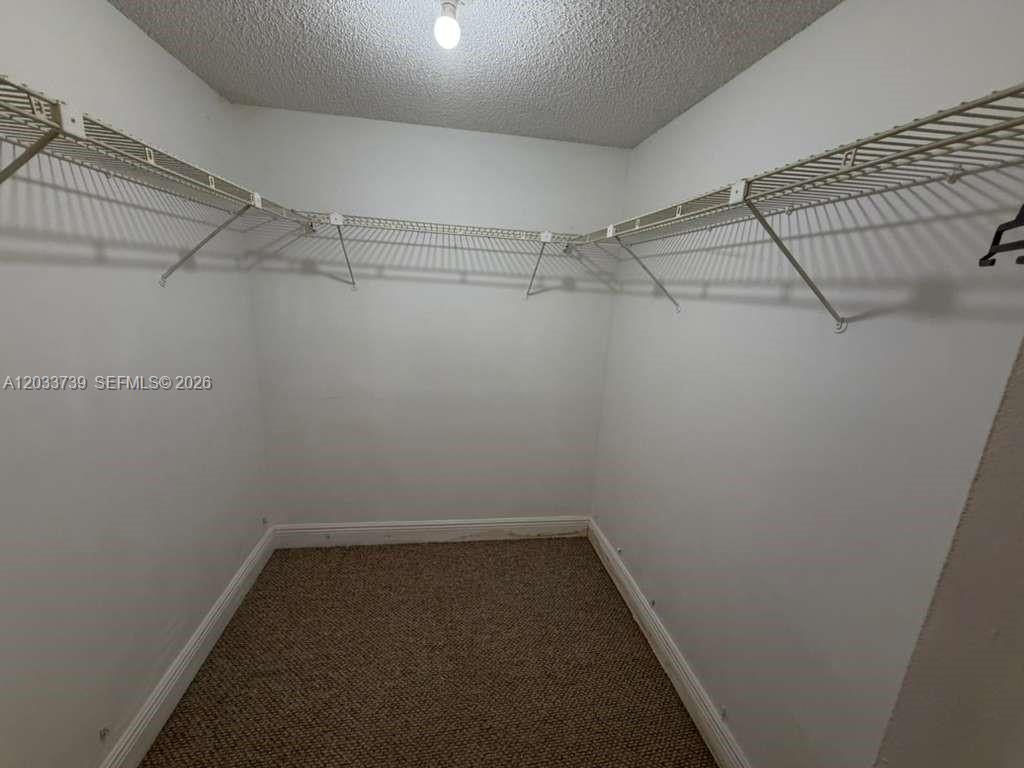 A walk-in closet features beige carpeting, white walls, and white wire shelving — 140 Lakeview Dr # 211, Weston FL 33326, WESTON, FL