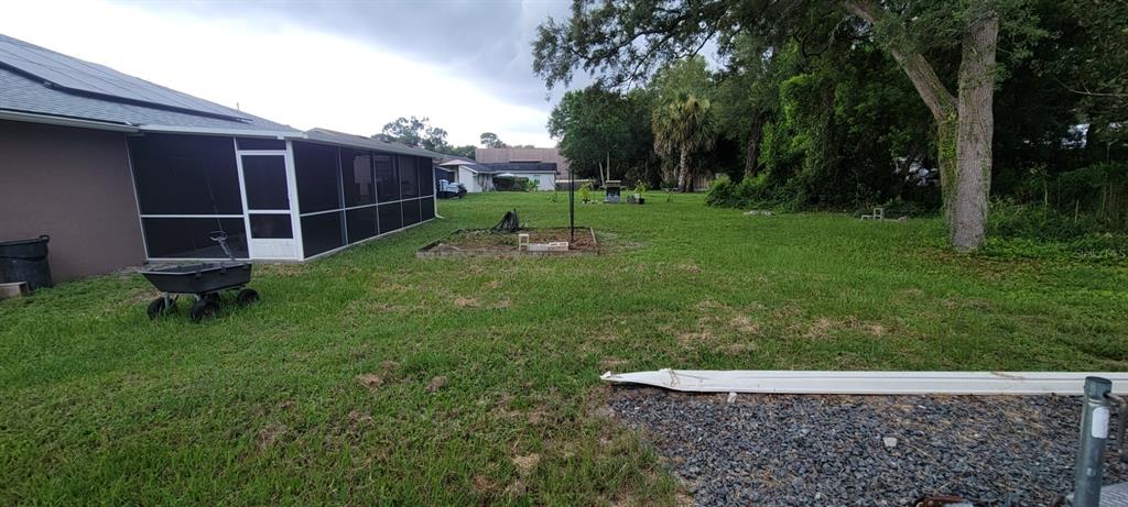 A backyard view featuring a screened-in patio, a small garden bed, and mature trees — 226 AGUA VISTA STREET, DEBARY, FL