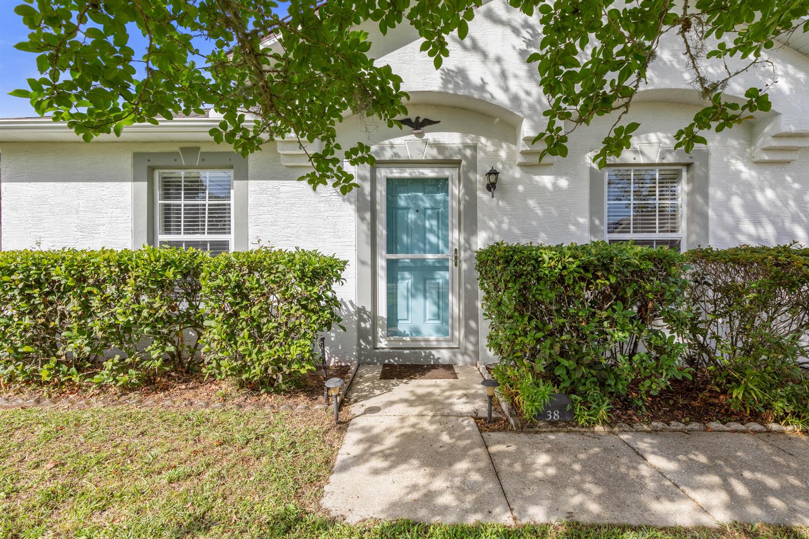 The exterior of a white house features a light blue front door and trimmed hedges — 38 Lloyd Trail, Palm Coast FL 32164, PALM COAST, FL