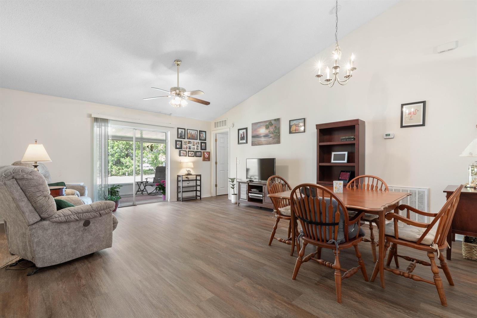 A living and dining area with wood-look flooring, vaulted ceilings, and a sliding glass door — 38 Lloyd Trail, Palm Coast FL 32164, PALM COAST, FL