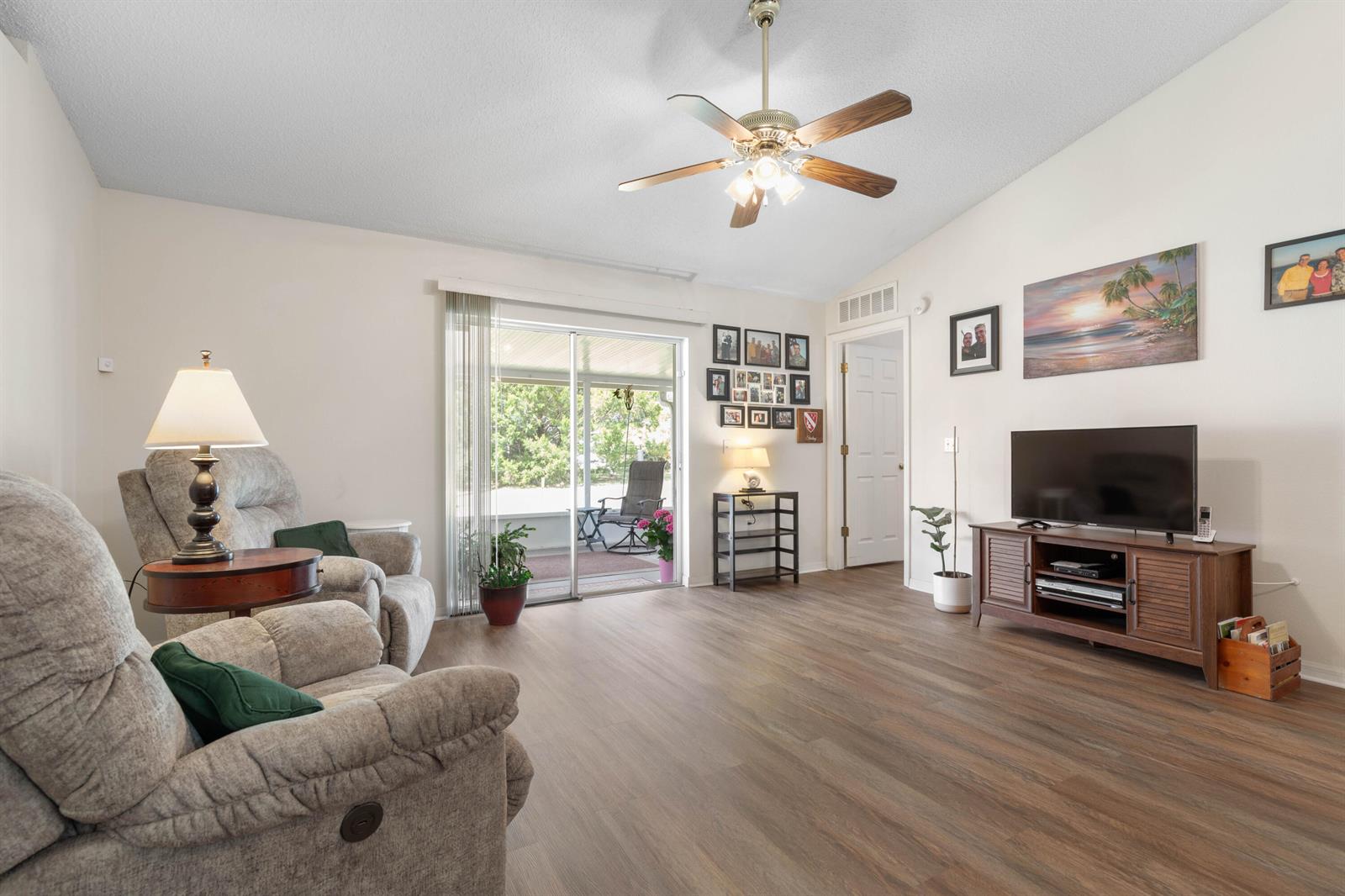 A living room features wood-look flooring, a ceiling fan, a television console, and sliding doors — 38 Lloyd Trail, Palm Coast FL 32164, PALM COAST, FL