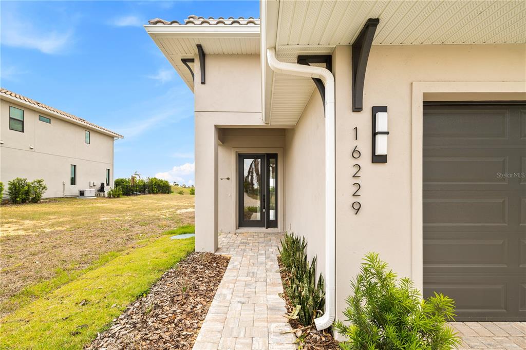 The exterior view shows a paved walkway leading to a front door and garage — 16229 RAVENNA COURT, BELLA COLLINA, FL