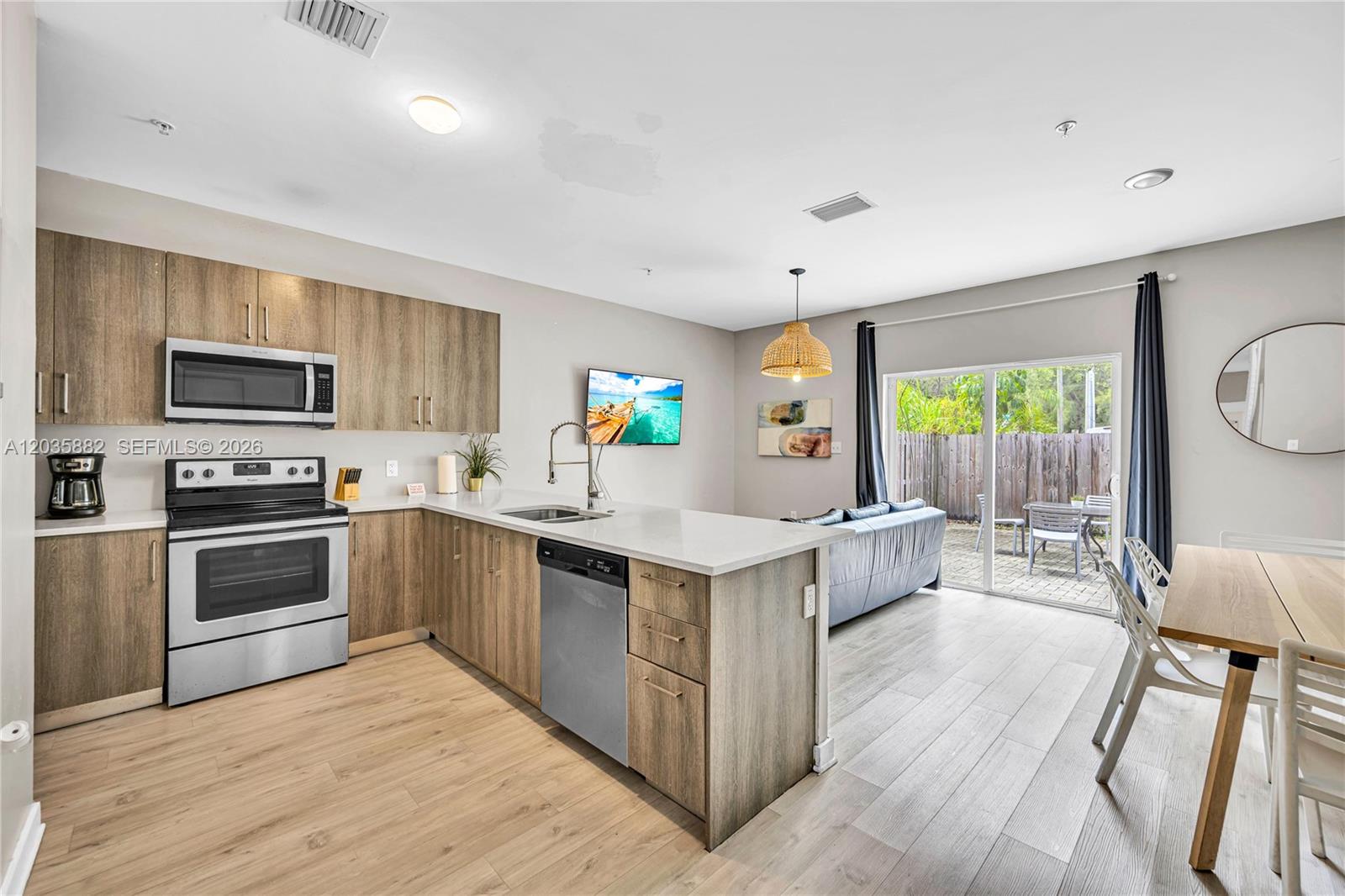 A living room with a black sofa, wall-mounted television, and an open kitchen with wood cabinets — 171 NW 158th St # 1, Miami FL 33169, MIAMI, FL
