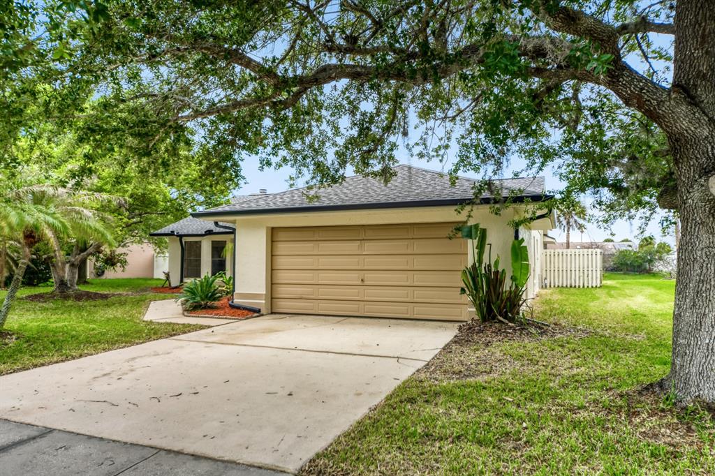 A beige house with a two-car garage and a concrete driveway under large oak trees — 2627 TALON COURT, ORLANDO, FL